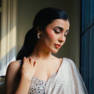 Woman in a silver dress with classic diamond hoops standing by a window 